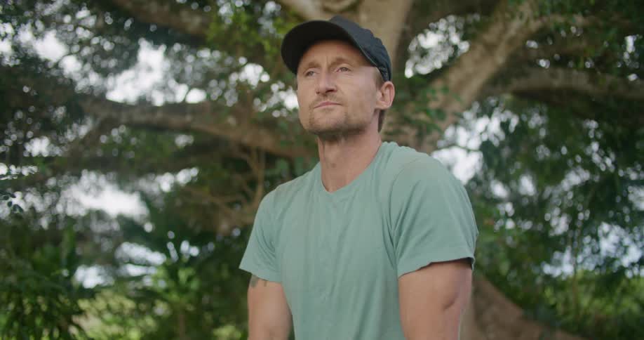 A man stops shoveling in the forest and looks up to take in the scenery