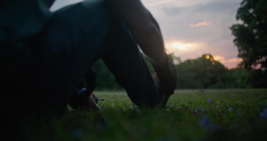 Man brushes off boot and places shovel down as he sits in field facing red sky