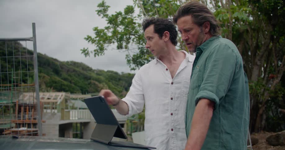 Two men talking while looking at a computer screen outdoors on a summer day