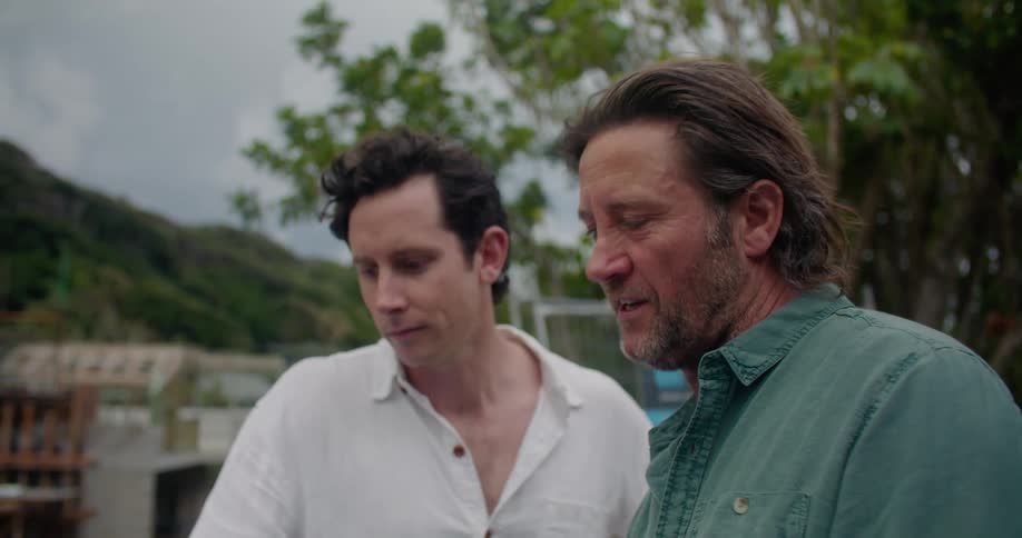 Two men look at a tablet outside and talk