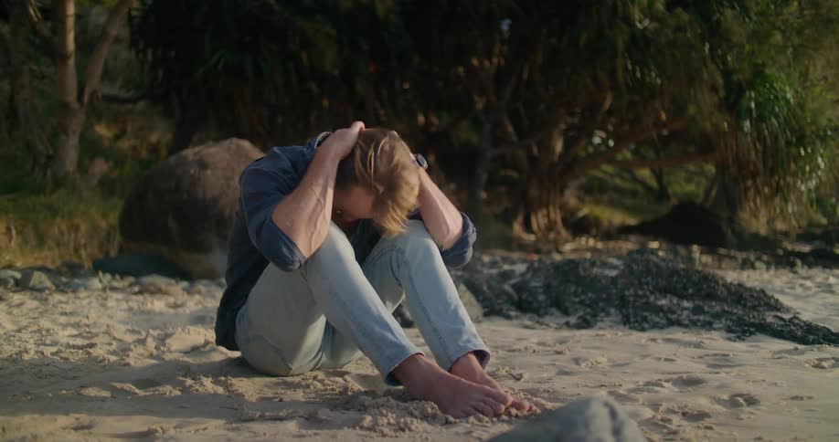 A man looking sad sitting on the beach