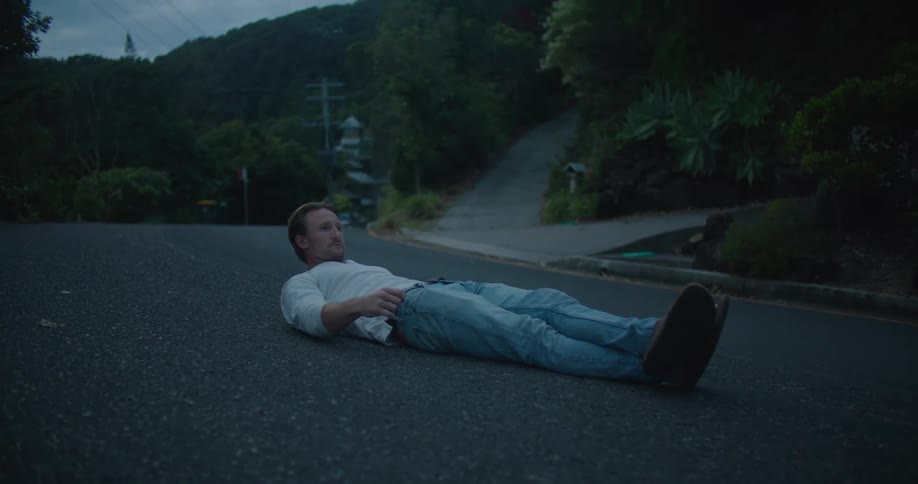 Man lies on his back in middle of road near driveways