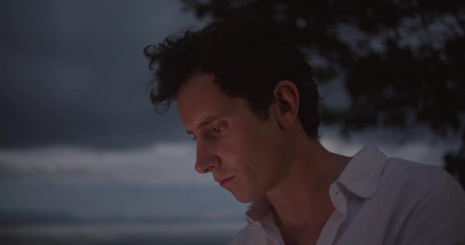 A man is outdoor holding and scrolling on a cell phone near the ocean