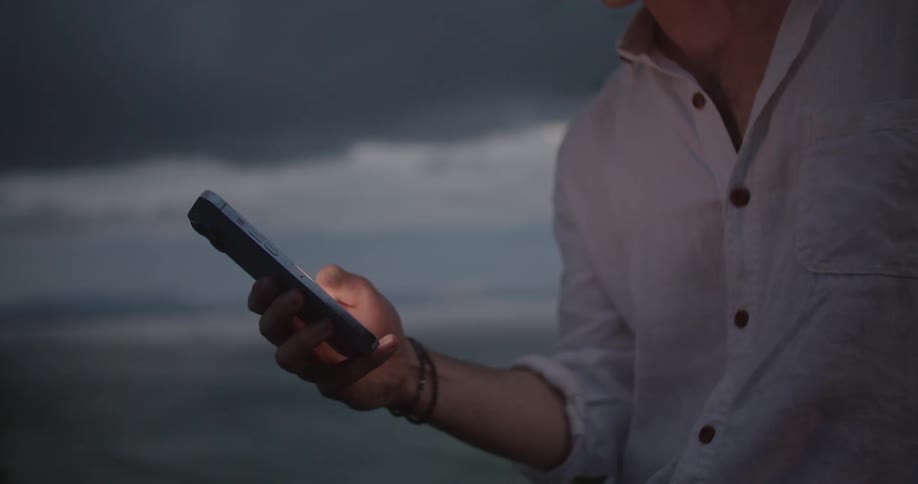 A man is standing outside using a smartphone at dusk