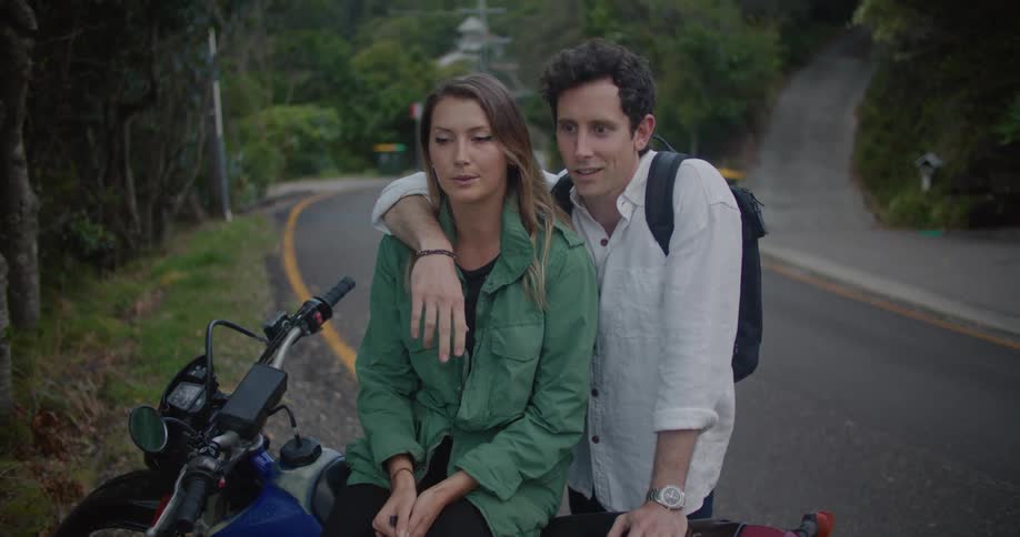 Couple hug and talk while sitting on motorcycle parked near intersection of road and driveways