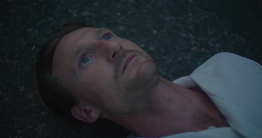 Man lies on his back on asphalt surface and stares