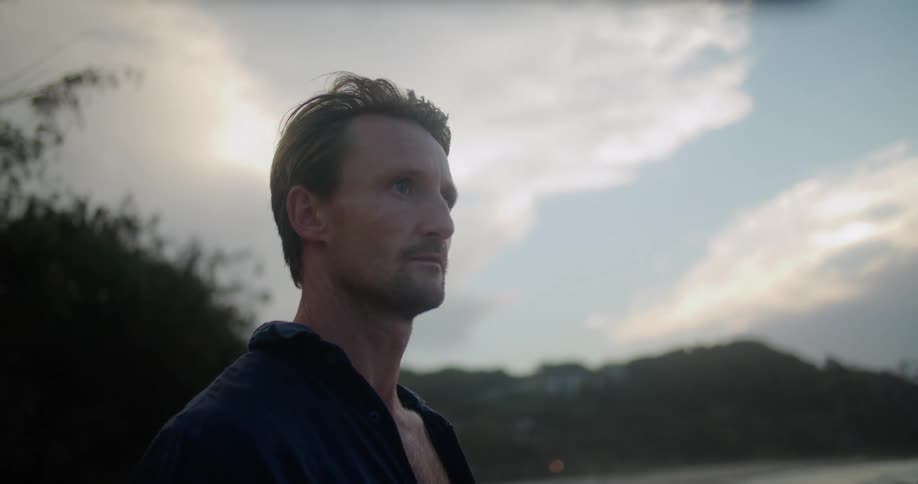 A man is standing outside looking ahead and there are trees in the distance behind him