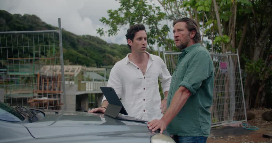 Two men stand near construction site gesturing and talking near computer set on car hood