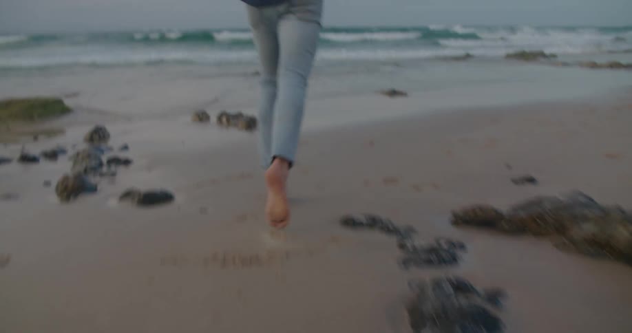 A man is jogging barefoot on an isolated beach littered with seaweed during the evening