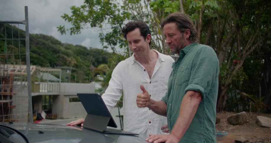 Two men standing outside talking on a tablet