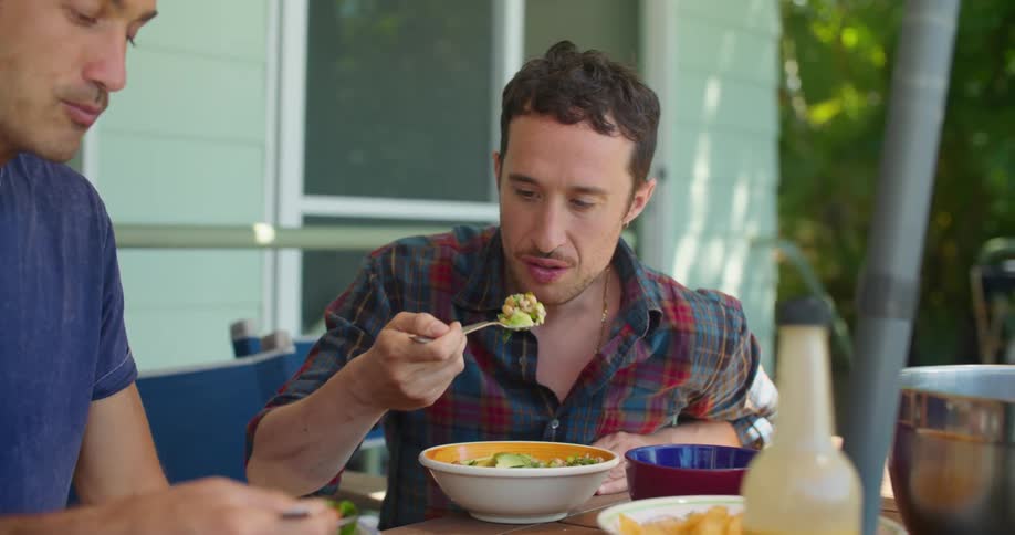 Two men sit together at a patio table eating