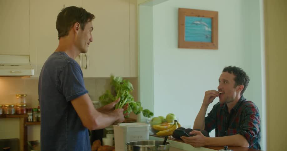 Two men talk and laugh as one cooks