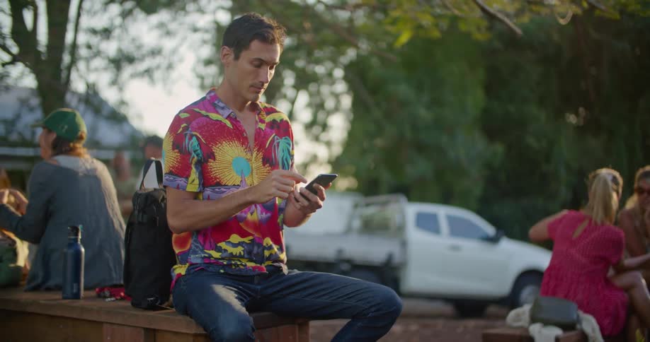 A man is looking at his cell phone as other people sit outside nearby