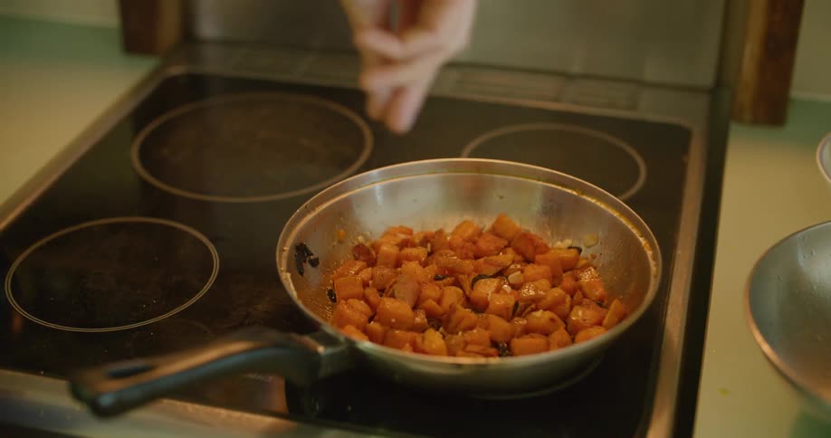 A person sprinkles seasoning on a hot pan of food