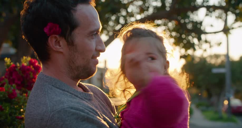 Father with flower behind ear holding her happy daughter on the neighbourhood at sunset