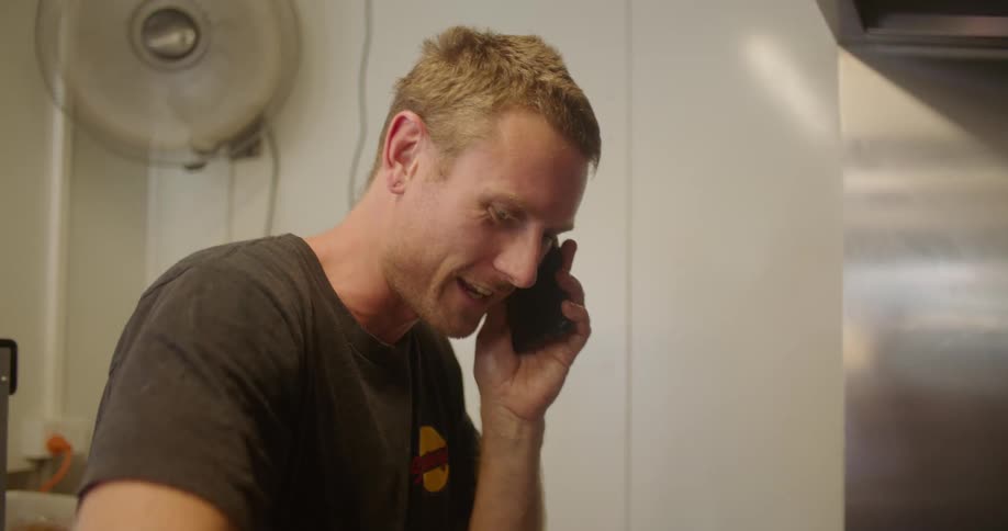 A man cooking in a kitchen at a restaurant while talking on a phone