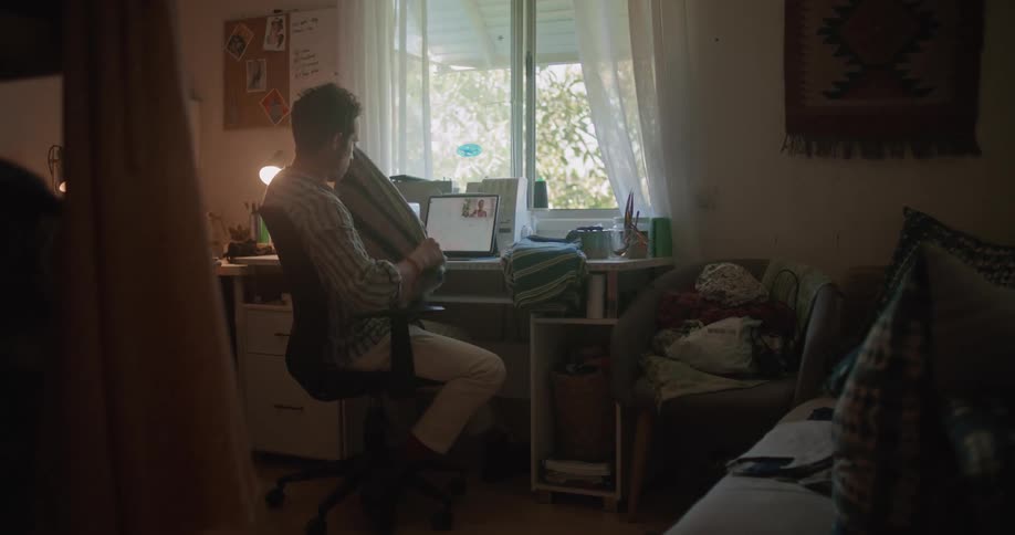 A man is folding clothes while talking on the computer with someone