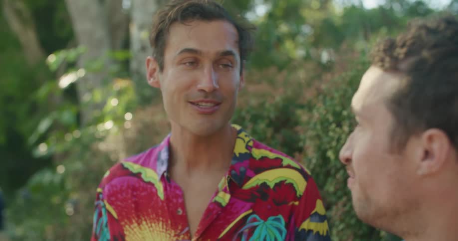Two men stand outdoors laughing and talking while they eat