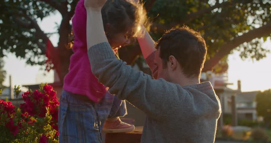 Father helps daughter to climb atop a wall in the backyard at sunset