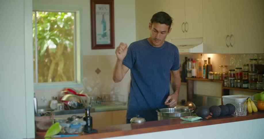A man bends to smell the aroma in a pot then turns to the stove to stir food in a pan