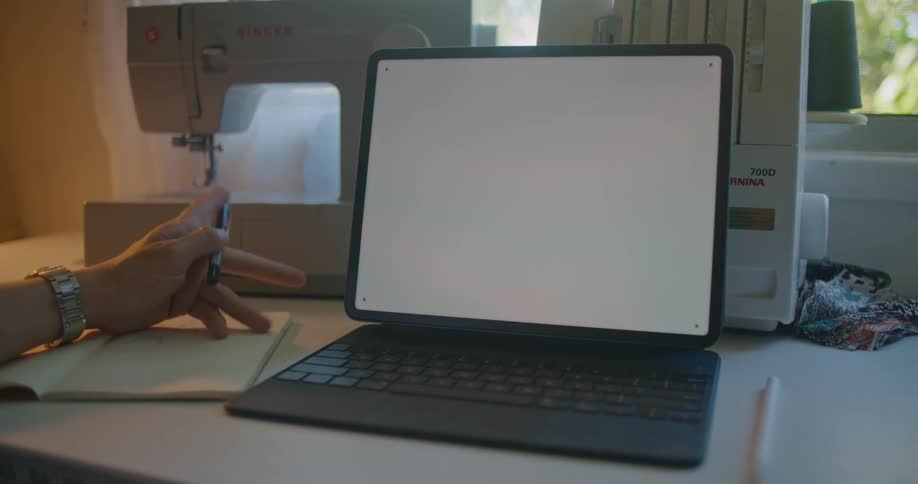 Person sits at table with notepad computer and sewing machine