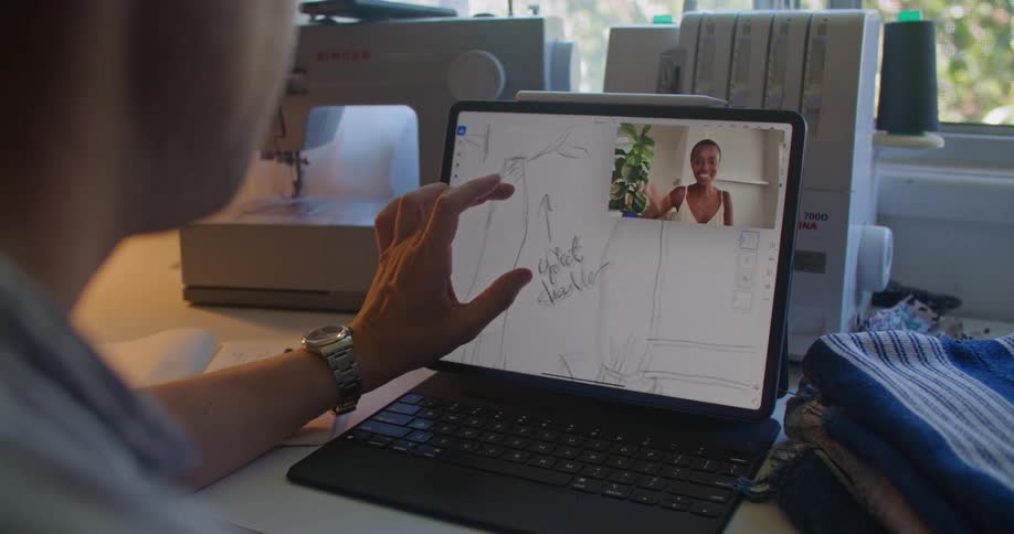Man sitting on a sewing workshop at home checking patterns on a laptop while talking on a video call