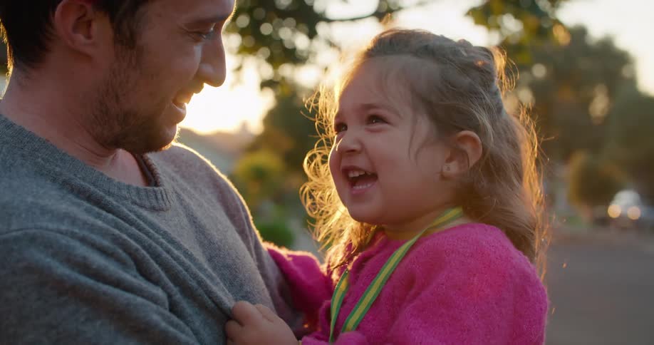 A man holds his toddler aged daughter as they stand outside their home