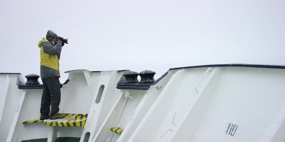 Man on a ship takes pictures while it snows