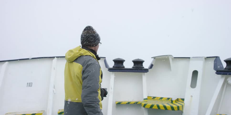A man walks along a ship as it snows