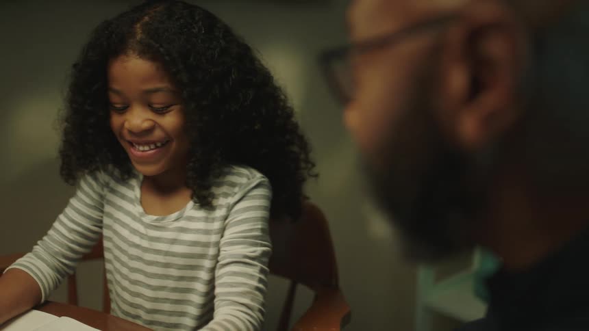 Father helping daughter with homework while sitting on the dinning table at home