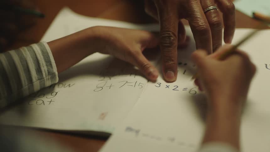 A father is helping his daughter do her math homework at a table in their home