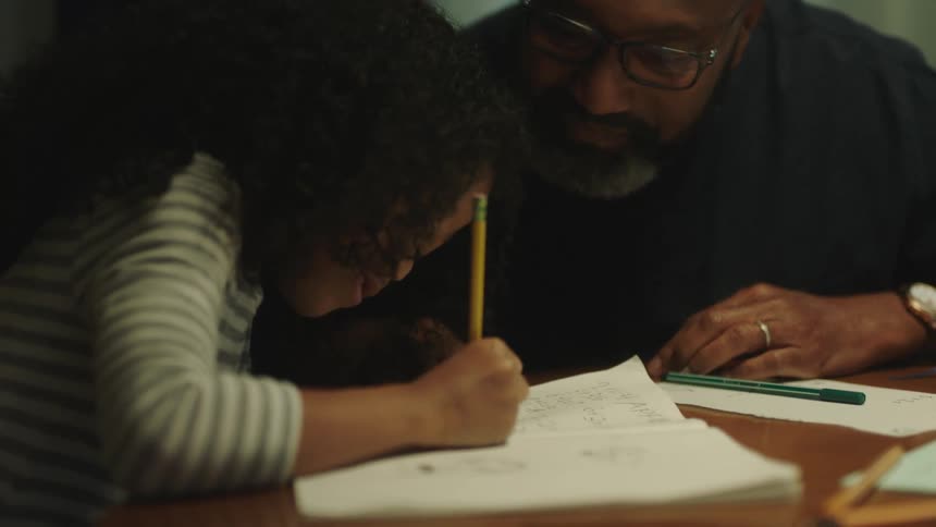 A father is watching his daughter do her homework at home and congratulates her with a fist bump