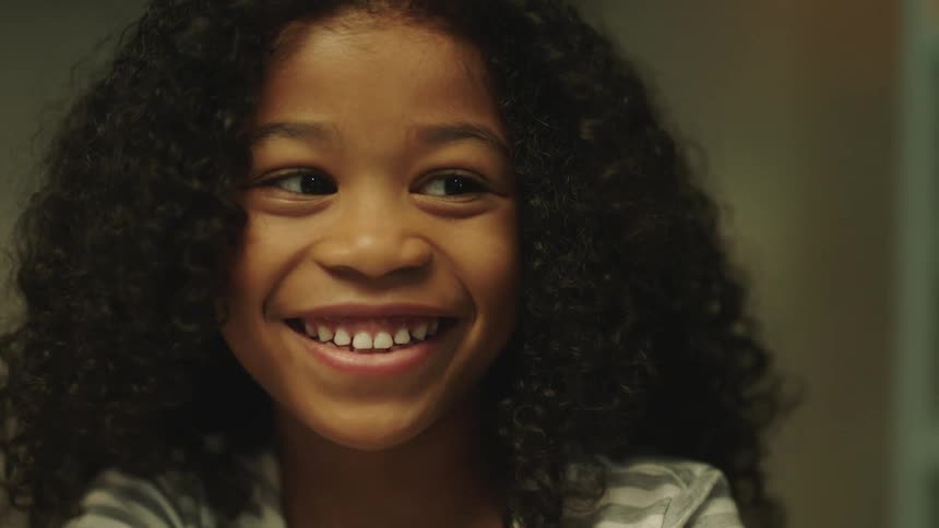 A young black girl is looking over to her side and smiling