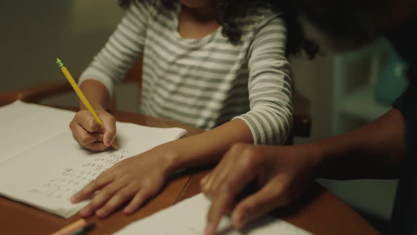 A girl sits with her parent and writes homework in a notebook
