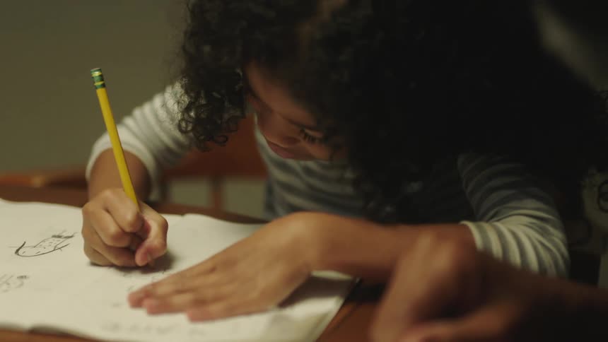 Father sits at table observing daughter complete homework