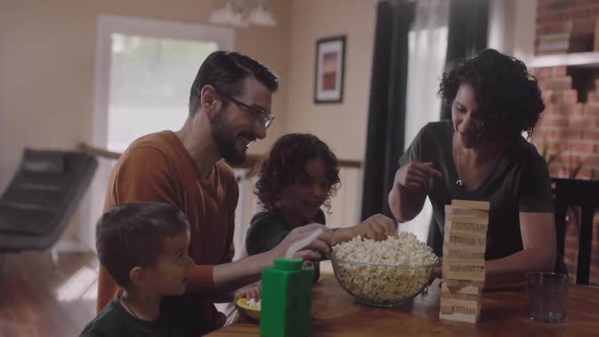 A family of four are sitting at a table with a bowl of popcorn in their home getting ready to play a game in the daytime