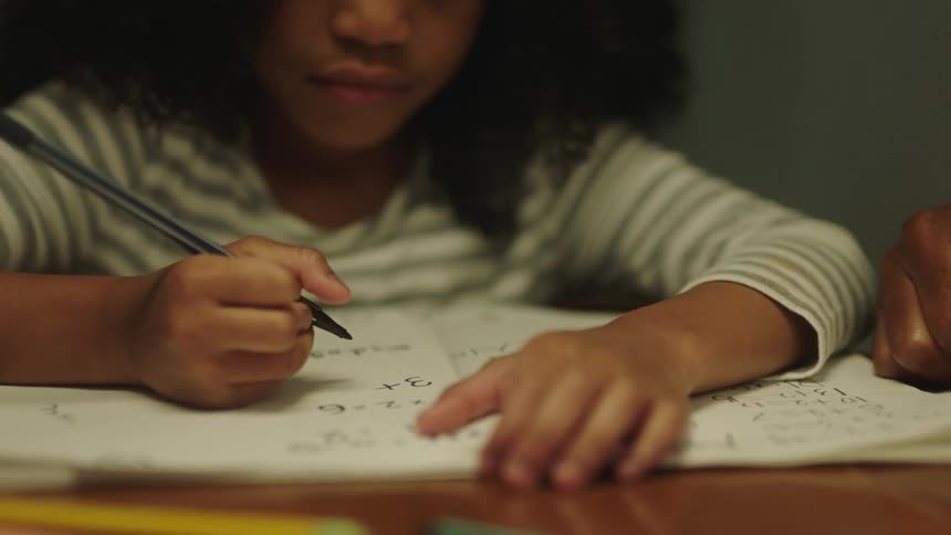 Girl with curly hair sits at desk and writes down in notebook next to man