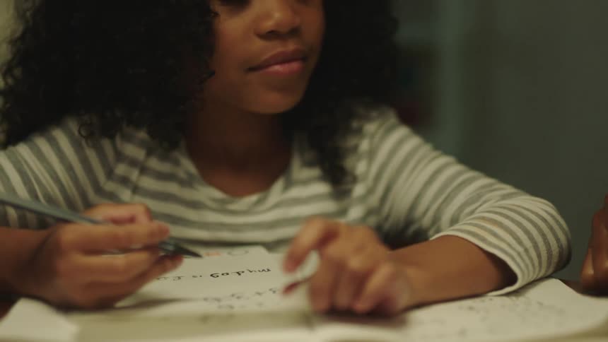 A little girl holding a pen looks up and listens to an adult giving instruction beside her