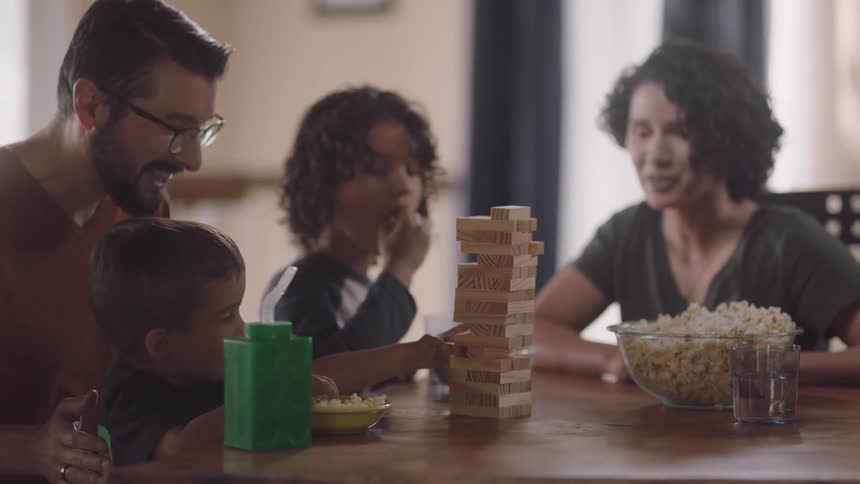 A woman claps and cheers on her son as he removes a piece from a block stacking game