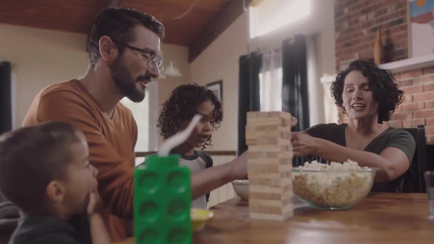 Parents sitting at the table at home playing with theri sons while eating popcorn