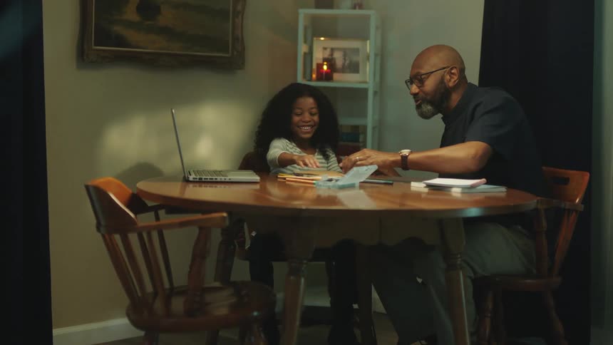 Father sitting on the dinning table helping daughter with homework