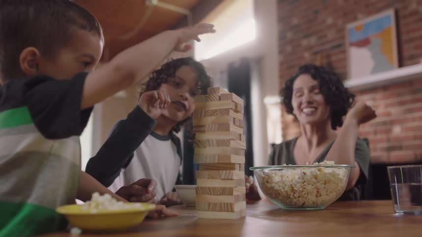 Happy parents playing jenga and eating popcorn with their children at home