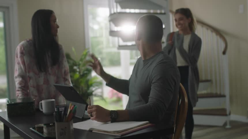 Man working at home talks to a friend while saying hello to a girl coming down a spiral staircase