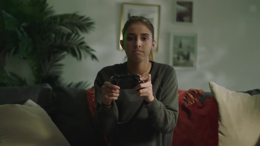 Young frustrated woman sitting on a couch at home playing video games with a controller