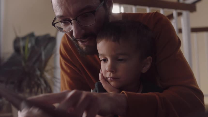 Father reads a book to his son while sitting on the floor of the living room