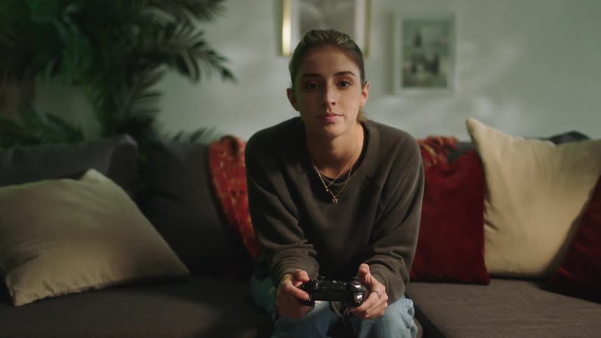 Young woman sitting in a couch at home playing video games with a controller looking at the camera