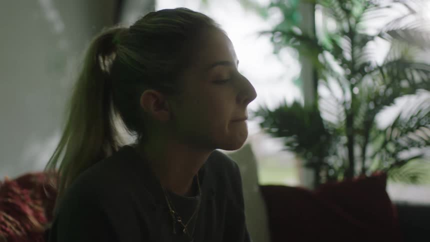 A woman in her 20s emphatically shakes her had no while sitting on a couch inside a room