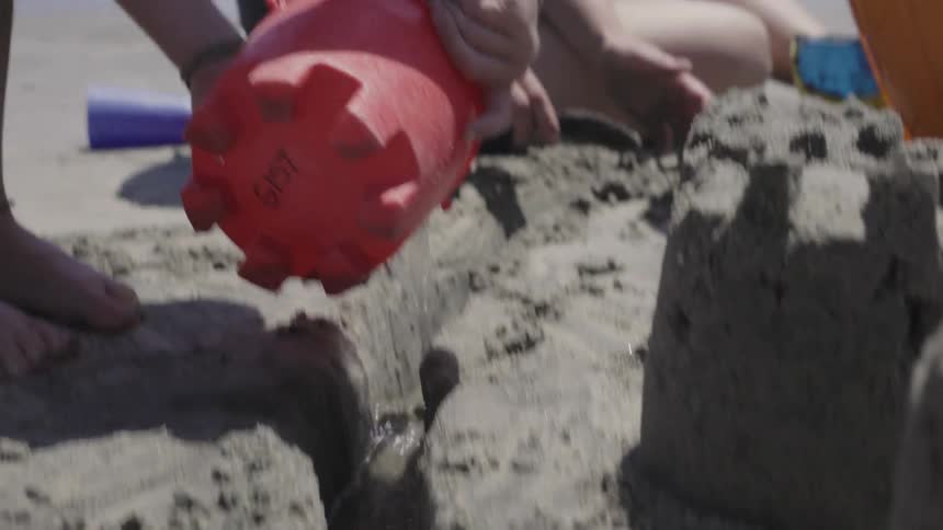 A child pours water in a small sand canal on the beach