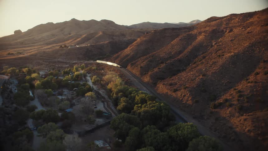 Aerial view of a train passing a small town in the mountains at sunset