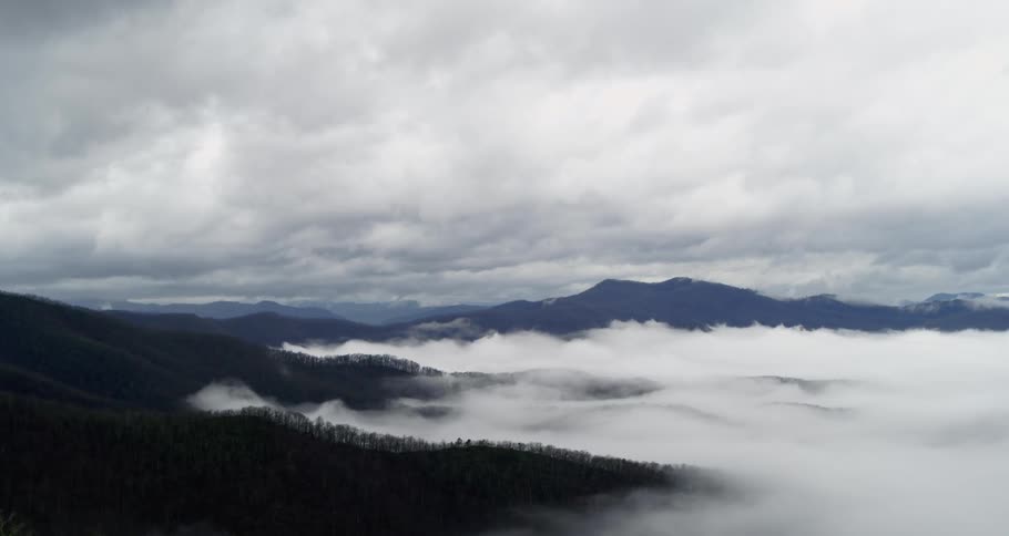 Clouds move over forested mountains high in a cloudy sky